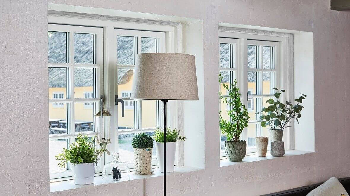Vinduesparti med hvide rammer og små indsatsvinduer, indretning med planter og støjsvag lampelys.