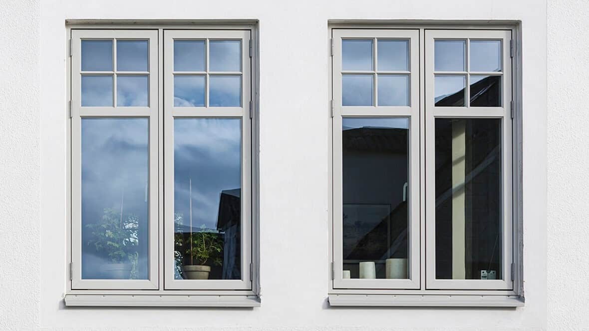 Reflekterende vinduer med hvide rammer på hvid facaderet væg.