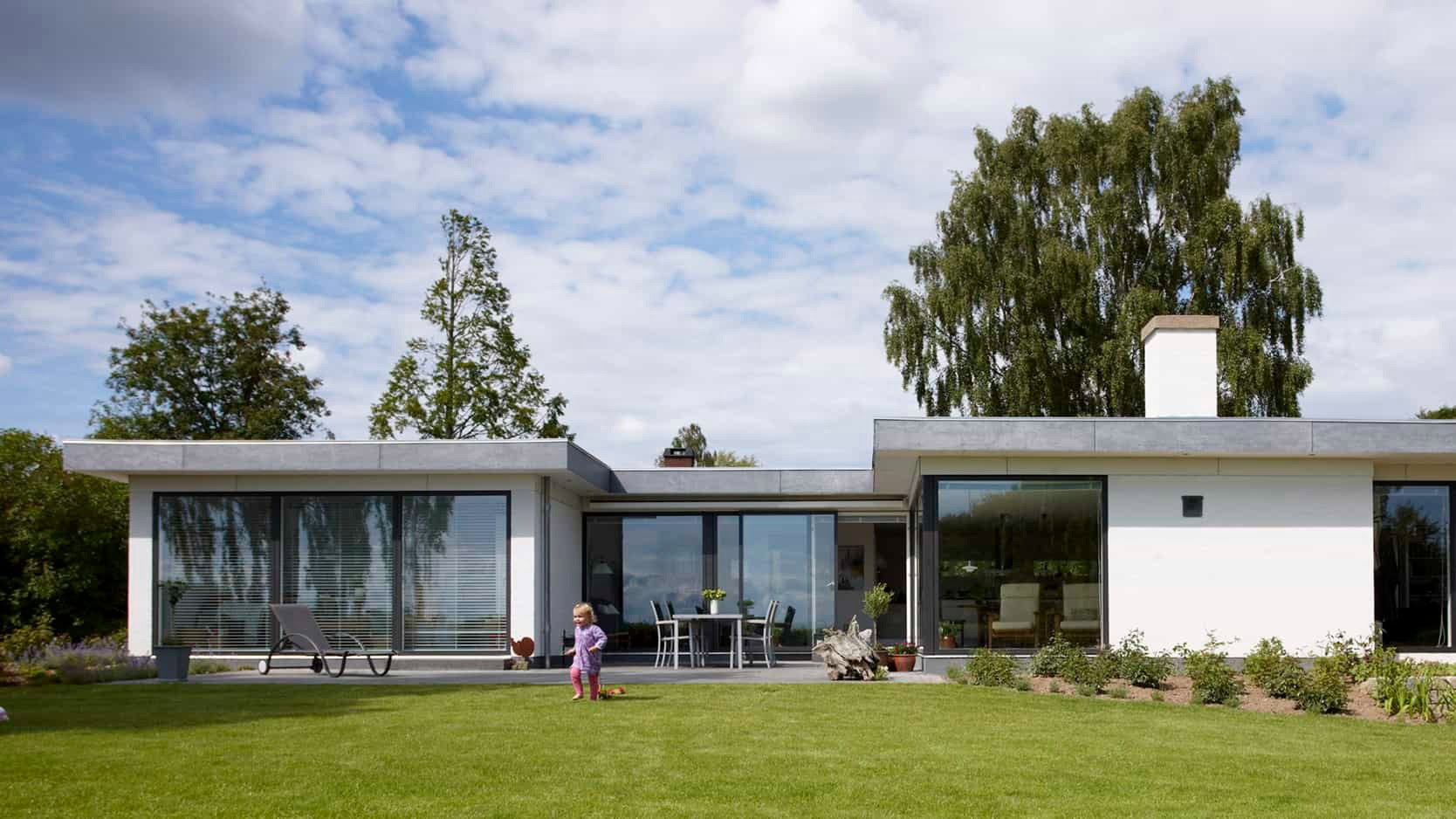 Billede af moderne boligareal med store vinduer og grøn have.