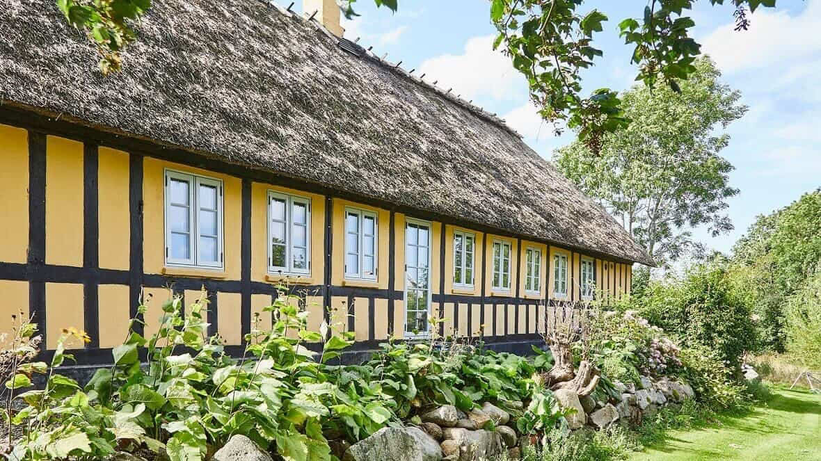 Håndlavede trævinduer i klassisk landstil med gul væg og stråtag.