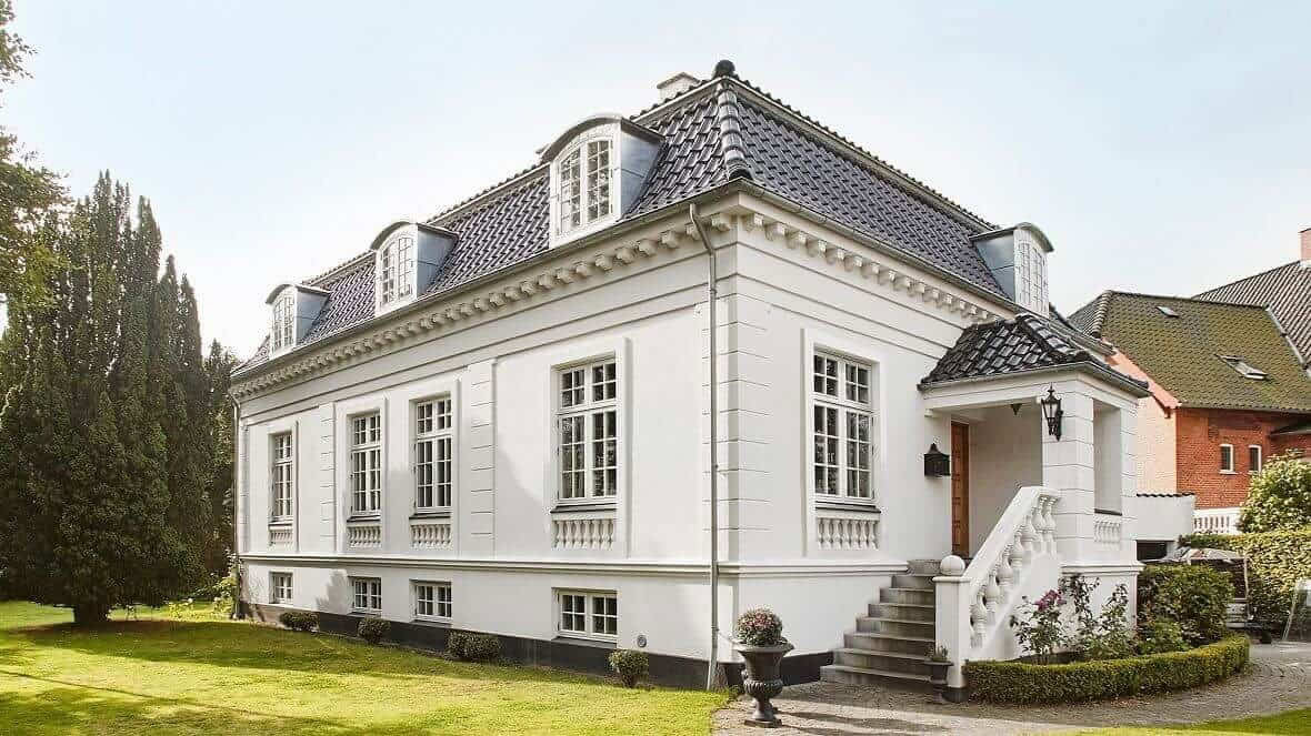 Moderne hvide villa med store vinduer og klassisk arkitektur i naturskønt område.
