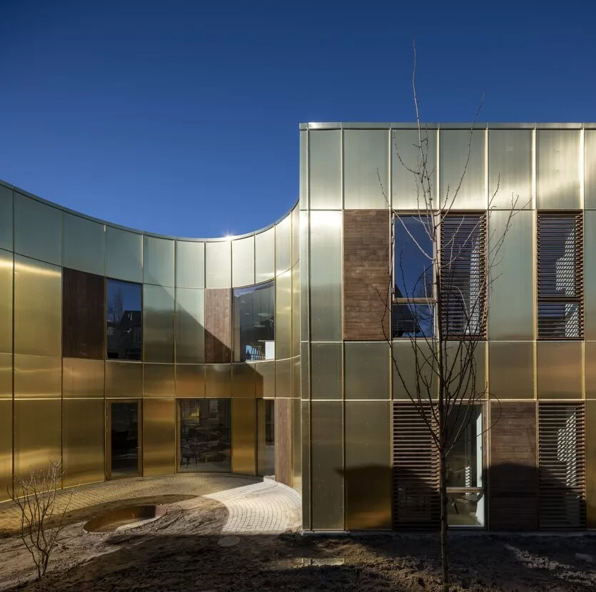 Moderne guldfarvede facader med store vinduer og trædetaljer på moderne bygning under blå himmel.