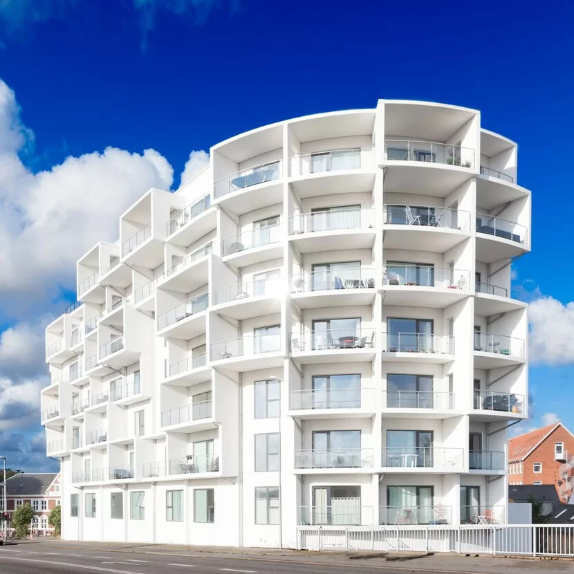 Hvide balkoner og store vinduer på moderne boligbygning, klar til at skabe lys og luft i hjemmet.