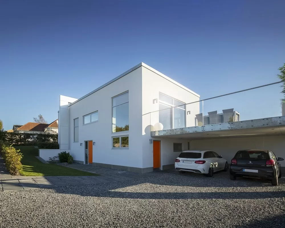 Hus med store, moderne vinduer og terrassedør under klart blå himmel.