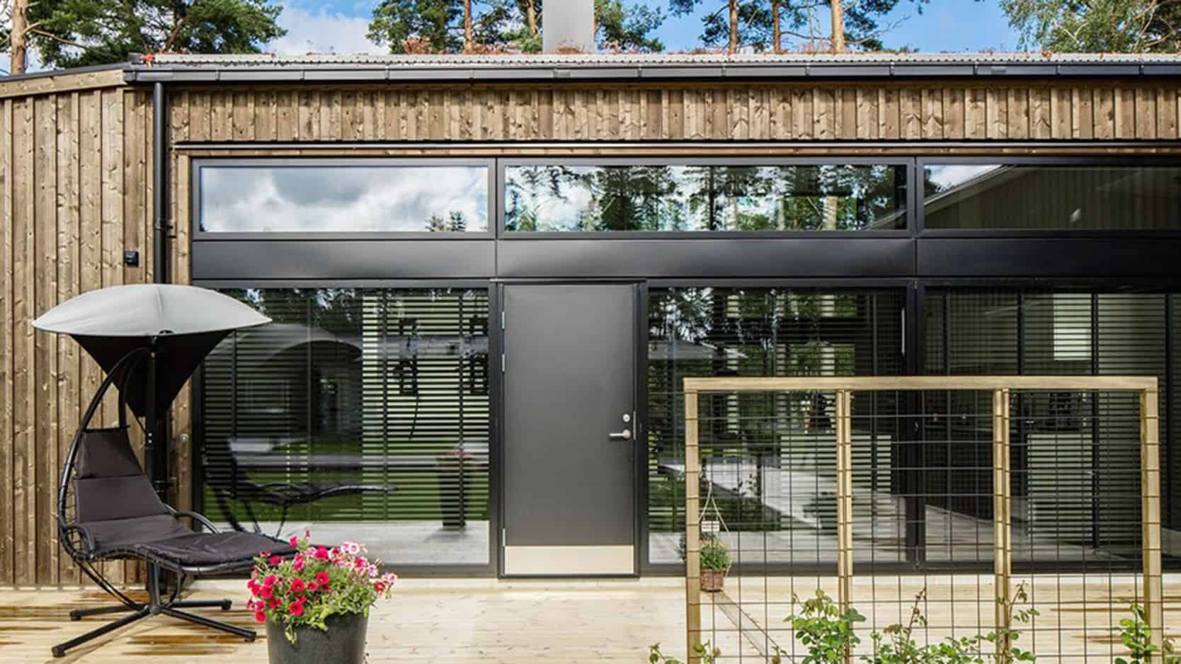 Moderne sort ramme af vinduer i træhusudside med stor terrasse og udendørs siddeområde.