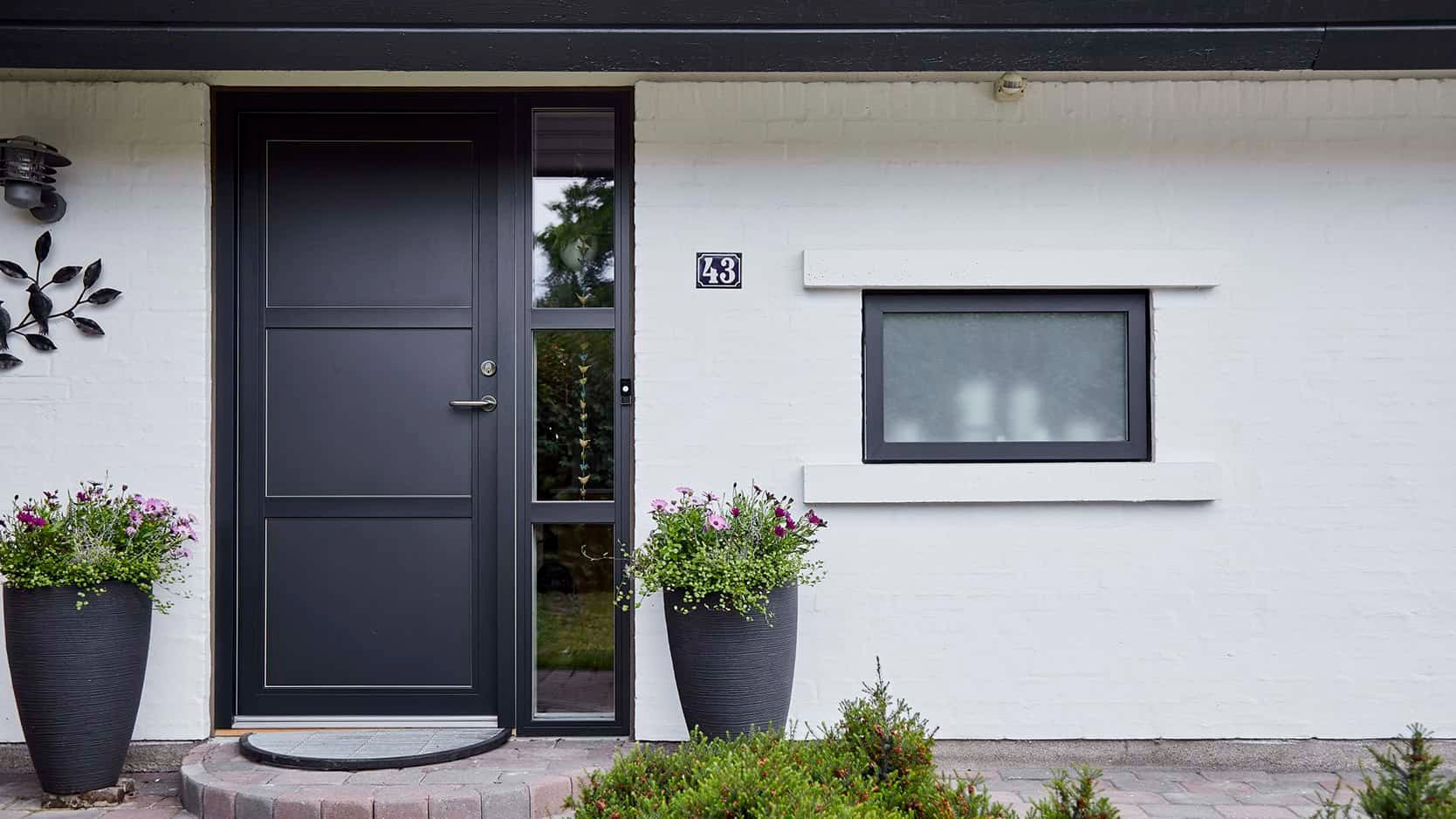 Elegante sort dør med sideglas og blomsterpotter foran, moderne og indbydende husfacade.