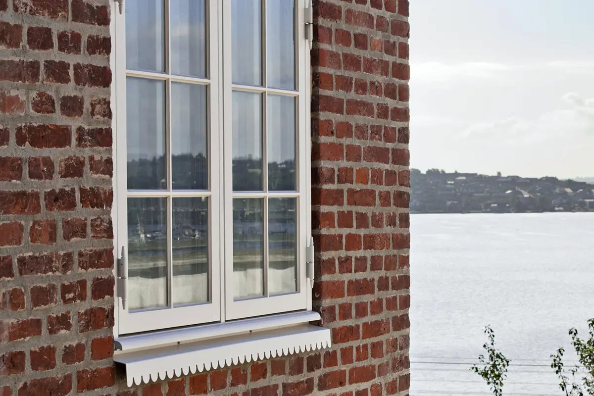Hvide vinduer ved vand med udsigt over fjorden, i rustikke røde mursten.
