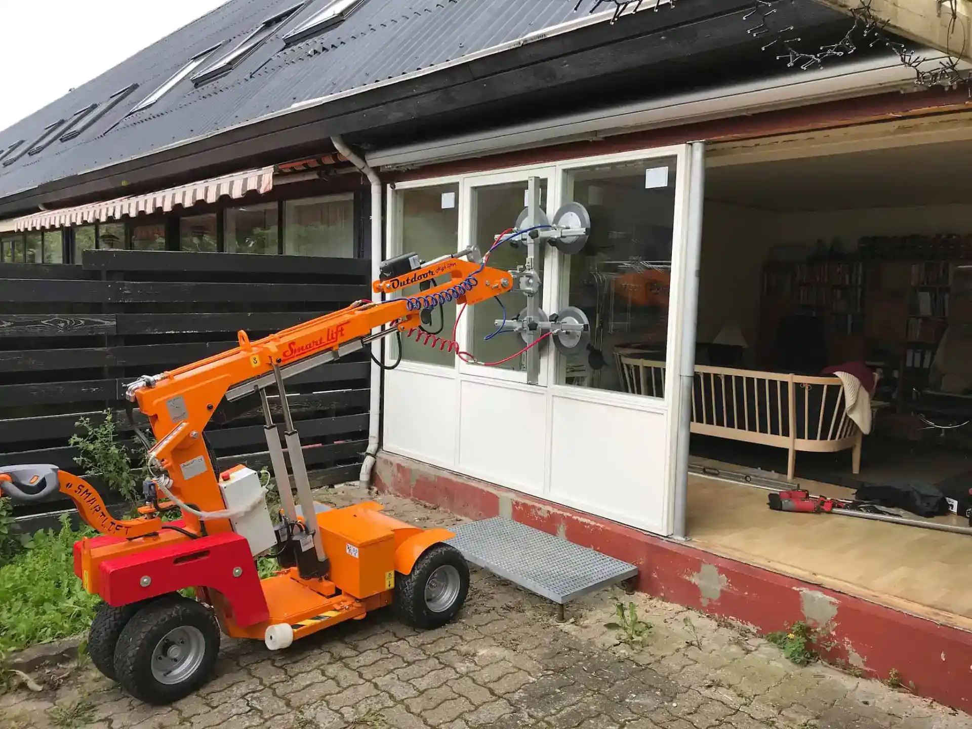 Højdejusterbart vinduesmonteringsudstyr foran et hus med store vinduer og terrasse.