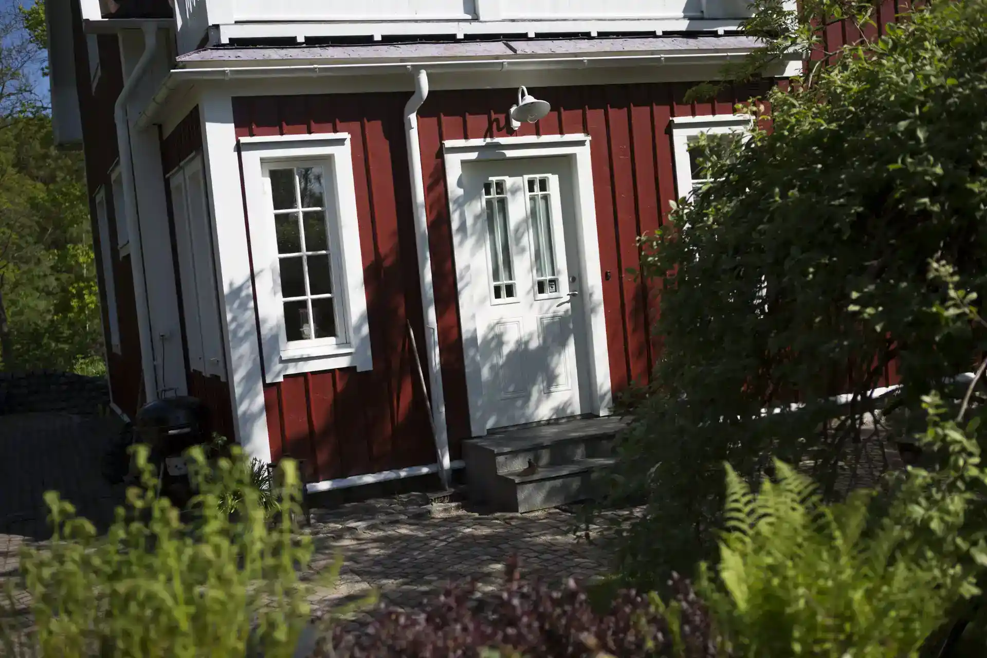 Elegant rødt træhus med hvide vinduer og dør, omgivet af grønne planter, perfekt til energieffektive vinduer.