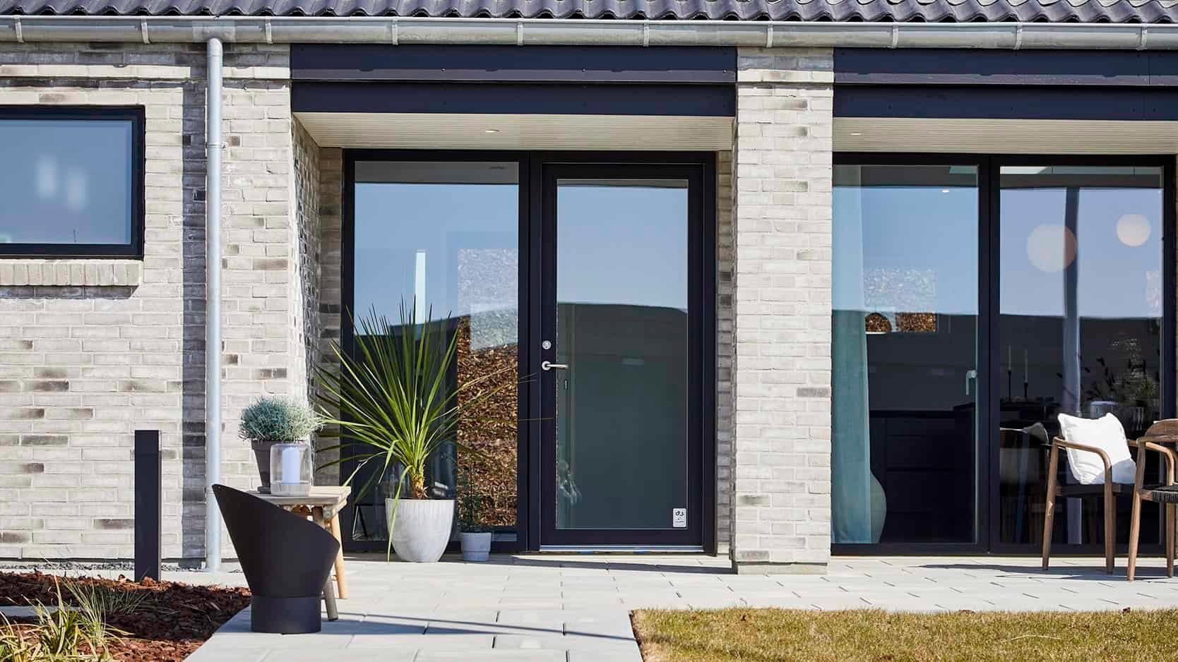 Flot moderne husfront med stort glasparti og sort træramme.