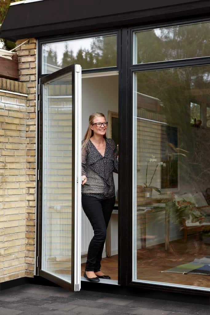 Nedvikbare glasdøre foran husfacade med kvinde i åbent rum.