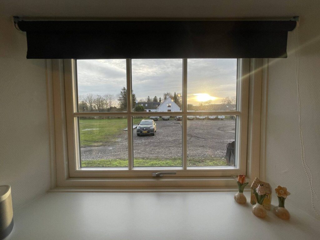 Klart vindue med landskabsudsigt og solnedgang i baggrunden.