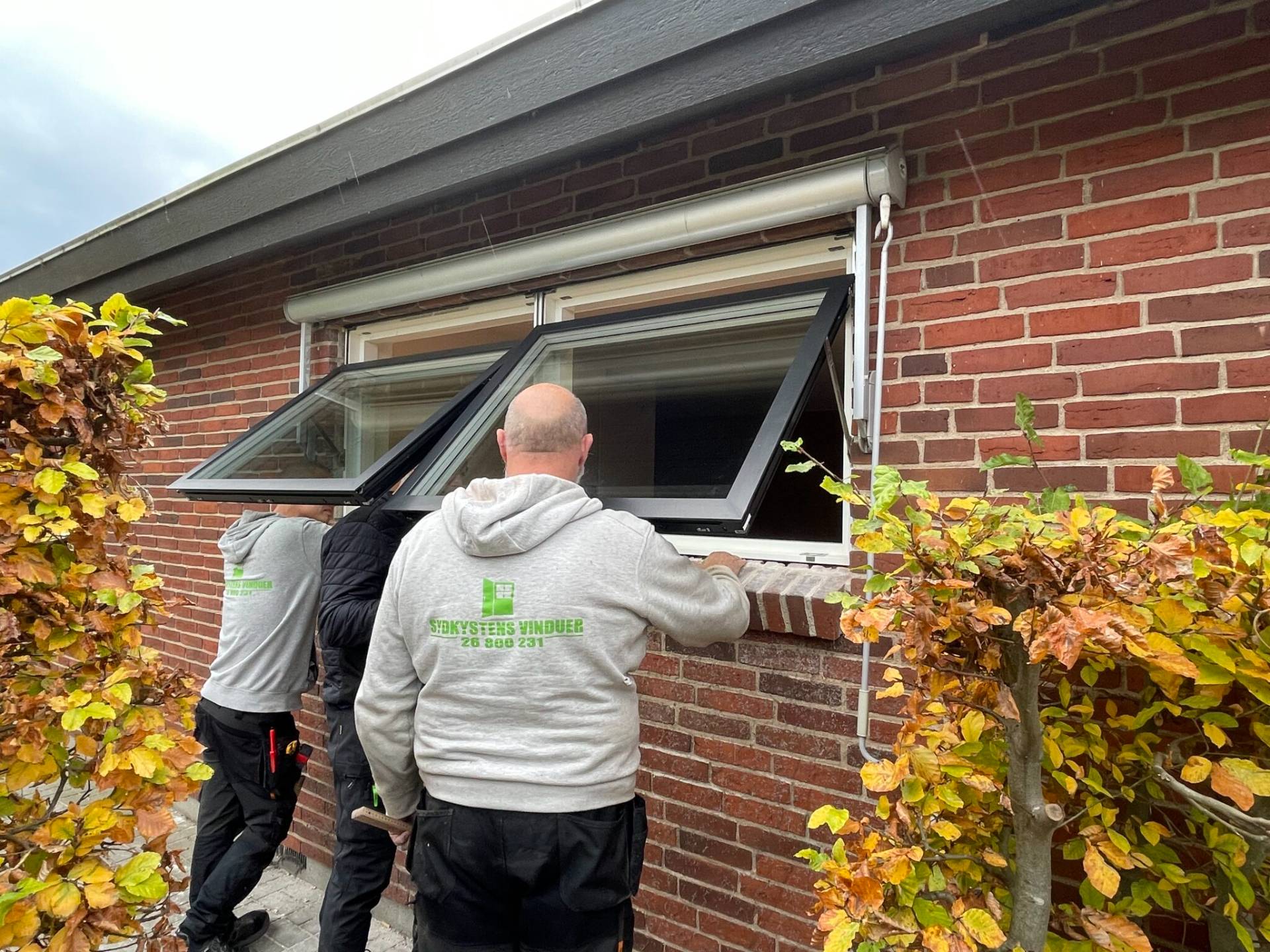 Højeffektivt vinduesudskiftning i gult murstenshus med tre installatører, der monterer nye vinduer.
